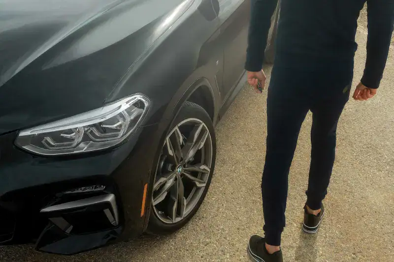 Person som går ved siden av en svart bil med nye dekk, klar for dekkbytte.